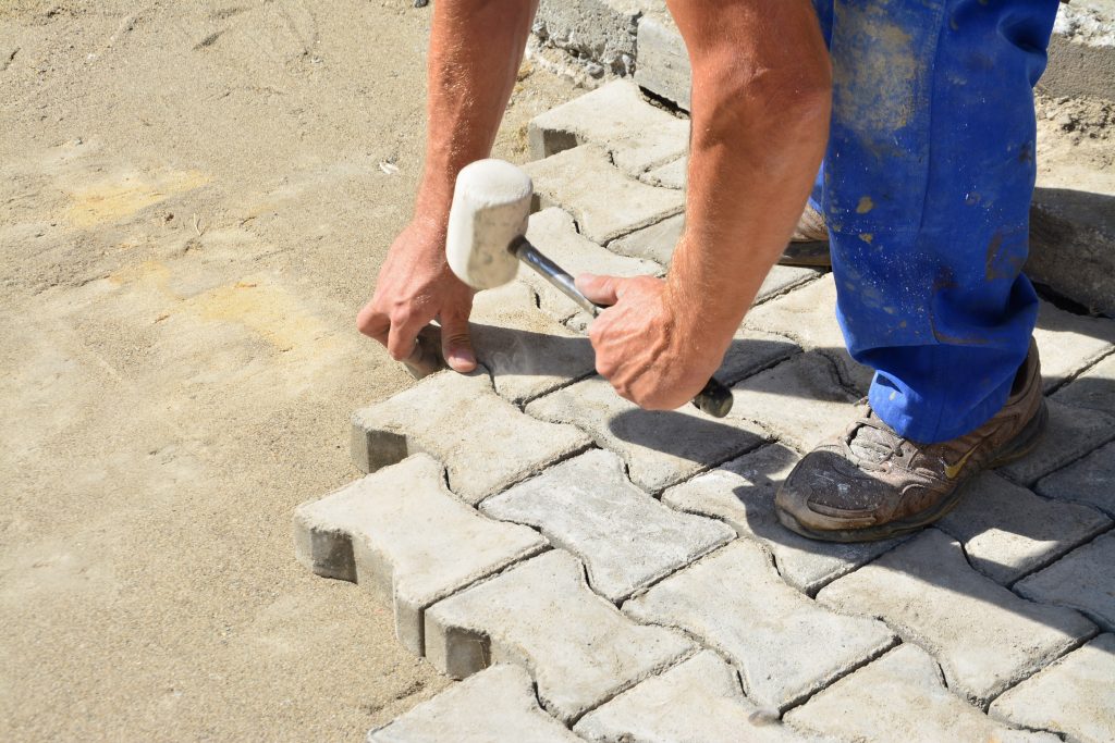 Worker laying concrete pavement onto the bedding sand and tapping them with a wooden hammer